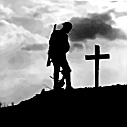 A soldier stands by a lone cross in silouette